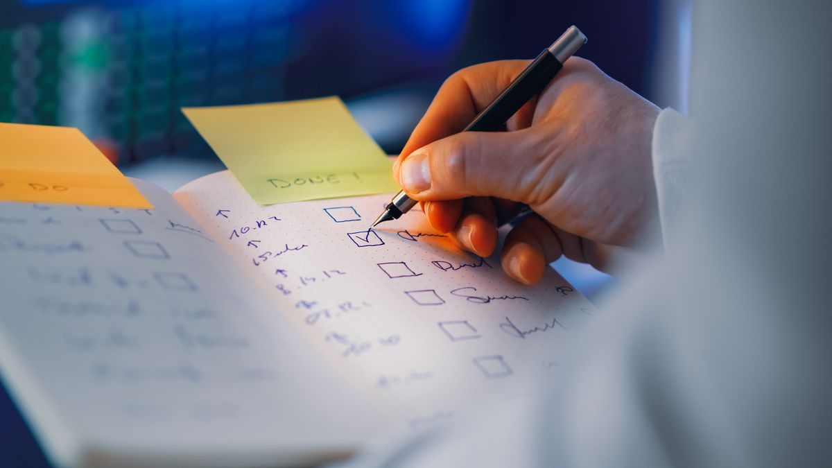 A close-up of a hand marking a checkbox with a pen on a handwritten checklist, next to a sticky note reading 'DONE'