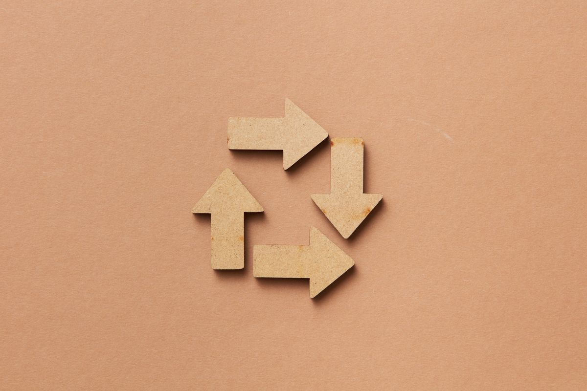 A recycling symbol formed from wooden arrows on a beige background, representing the reconnect-and-resend cycle that turns a failover event into an automatically retried write